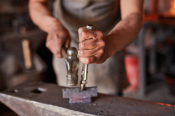 istock Workshop, blacksmith and hands with hammer for iron artisan product manufacturing and labour. Anvil industry worker crafting professional materials in work room with industrial steel tools. 1436445474