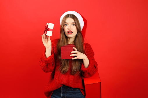 Young woman in New Year's clothes is upset with a Christmas gift, negative emotions. People on a red background.