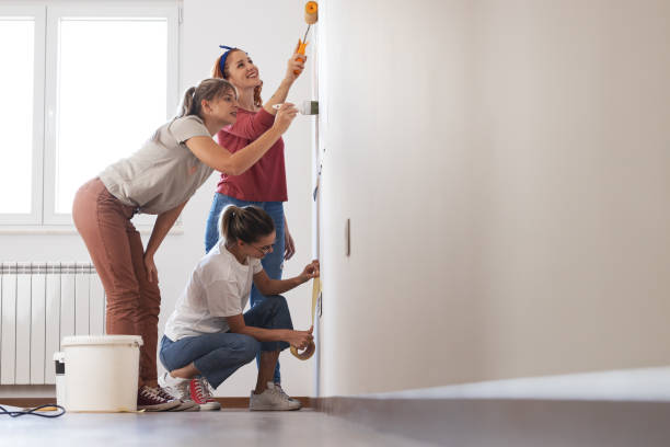 新しい家の壁を飾るためにペイントローラーを使用する女性のルームメイト。 - female house painter home decorator paintbrush ストックフォトと画像