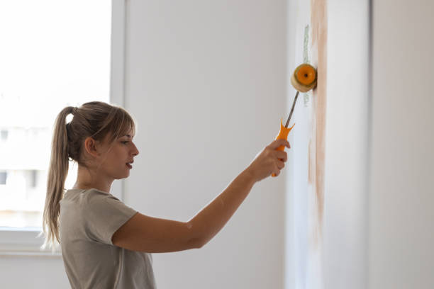 istock Young female using paint roller to decorate walls in her new home. 1436452173