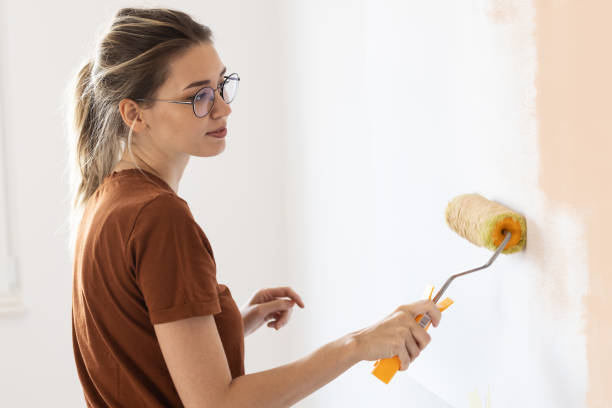 istock Young female using paint roller to decorate walls in her new home. 1436452174