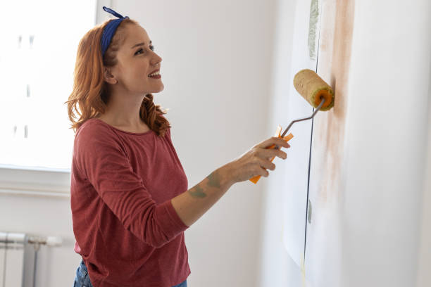 Young female using paint roller to decorate walls in her new home.