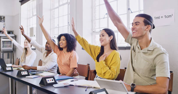 istock University classroom, students and ask question happy learning with hands up and digital tablet. Modern education, software teaching and excited college diverse men and women in seminar or lecture 1436453644