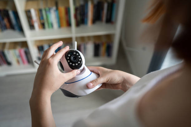 Close up on midsection and hands of unknown caucasian woman holding home security surveillance camera while standing in room adjusting and setting up equipment copy space stock photo