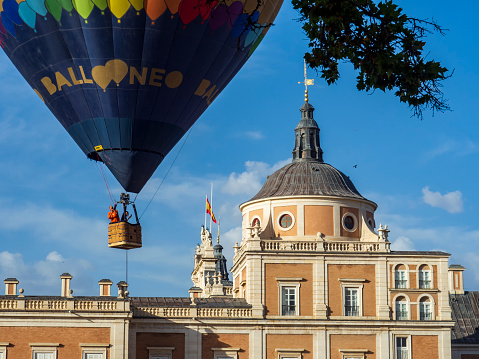 Aranjuez, Madrid, Spain. 10/08/2022 A basket with passengers of a hot air balloon rises with the palace of Aranjuez in the background, during the celebration of the traditional Aranjuez Hot Air Balloon Festival.
