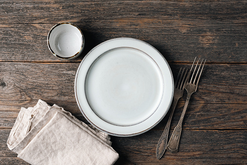 Empty plate, vintage silverware and linen kitchen textile on old wooden table. Rustic table setting, top view, copy space for text or design elements