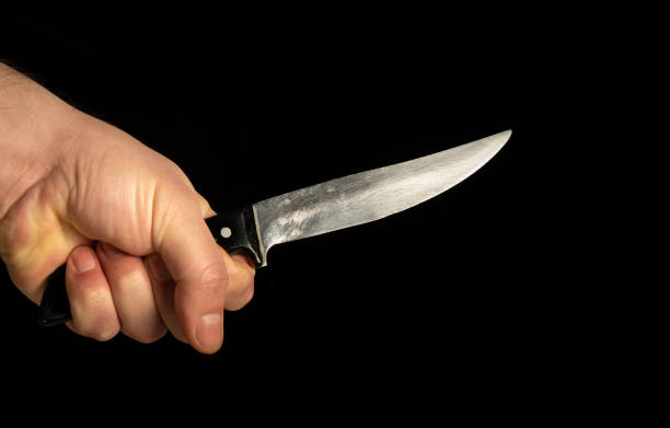 istock Closeup male hand holds sharp knife isolated against black background 1436457637