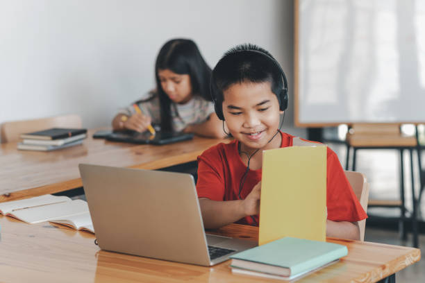 istock Elementary school boy with headphones. Distance learning online education. A schoolboy boy studies at home and does school homework. A home distance learning. 1436462892