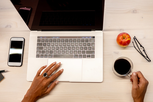 High angle photo of businesswoman's hands while using a laptop computer and holding a cup of coffee.