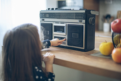 Toddler baby girl pressing play button on a boombox radio in home kitchen