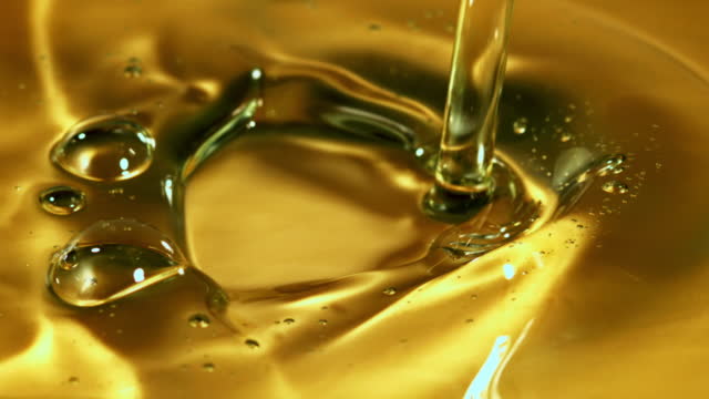 A jet of olive oil falls with splashes. Filmed on a high-speed camera at 1000 fps.