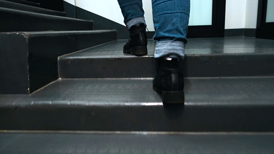 Close-up of feet climbing staircase. Concept. Beautiful feet in leather boots and jeans climb stairs in room. Woman quickly climbs stairs in building.