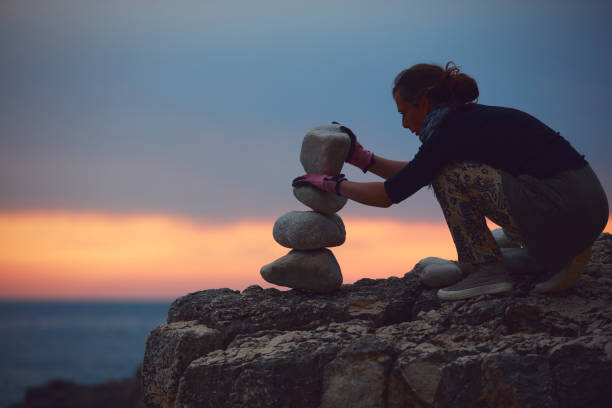 silhouette einer frau, die felsen und steine an der meeresküste bei sonnenuntergang balanciert. - stone stability balance zen like stock-fotos und bilder