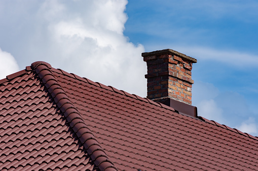 Roof made of metallic tiles with a chimney made of bricks against a cloudy sky