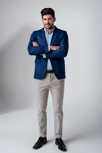 Full length studio shot of a handsome man wearing shirt and blazer while standing with arms crossed at isolated background. Copy space.