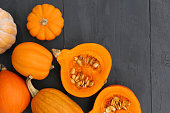 Cut orange Hokkaido pumpkin with seeds on black wooden background.