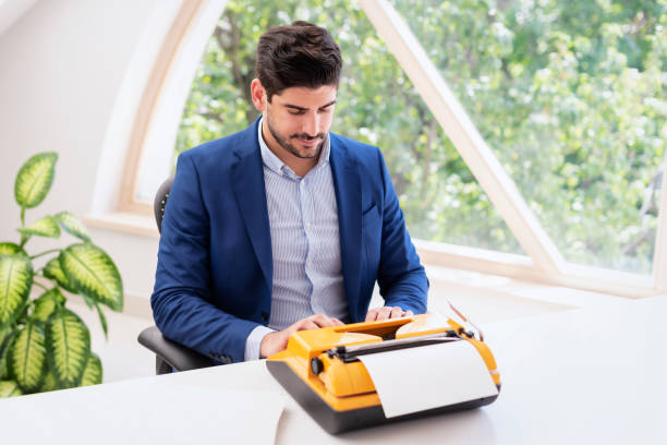 man sitting at desk and using retro typewriter - typewriter writing journalist typing imagens e fotografias de stock