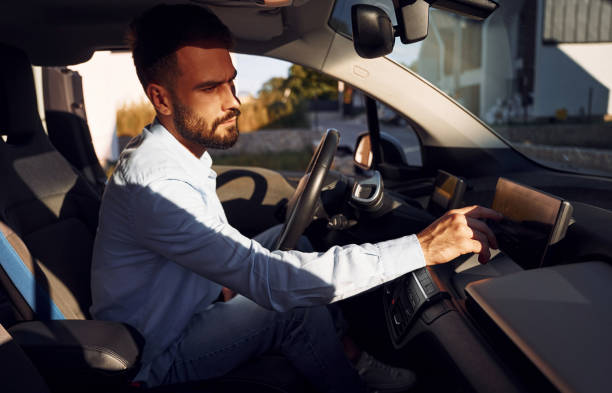 男は車の中に座っている。若いスタイリッシュな男は昼間に電気自動車を持っている - car driving inside of indoors ストックフォトと画像