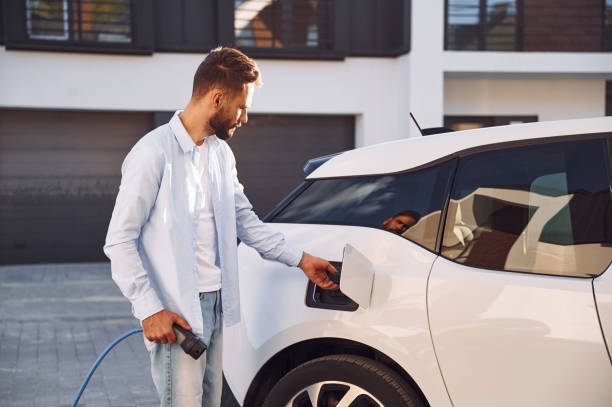 istock Plugging in charging cable. Young stylish man is with electric car at daytime 1436481950