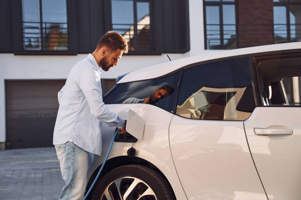 istock Plugging in charging cable. Young stylish man is with electric car at daytime 1436481958