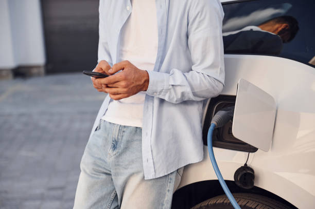 istock Standing with smartphone while automobile is charging. Close up view of man with his electric car 1436482082