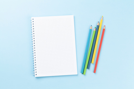 Blank notepad and colorful pencils. Flat lay over blue background with copy space