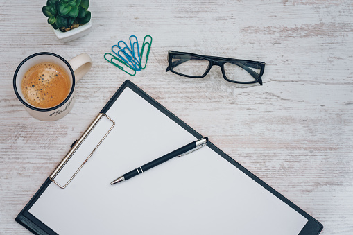 Clipboard folder with blank paper, strong refreshing coffee, reading glasses and small plant for comfort. Horizontal photo.