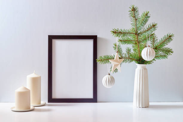 istock Mock up black poster frame with christmas decoration in home interior, scandinavian style. Green fir branches in a vase and ball on a white table 1436497183