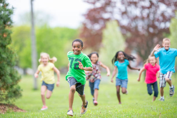 Camp Children Running A large group of school aged children run through the grass together during day camp.  They are each dressed casually in colorful t-shirts as they smile and enjoy the summer day. summer camp stock pictures, royalty-free photos & images