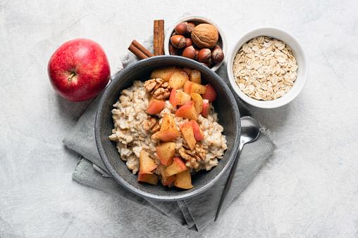 Oatmeal porridge bowl with cinnamon apples and walnuts on grey concrete background. Fall breakfast comfort food, top view, flat lay