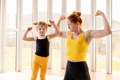Young fit mom and her daughter in matching clothes, showing muscles. Fitness motivation