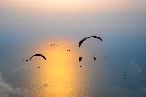 Many paraglider at sunset over the sea among the clouds