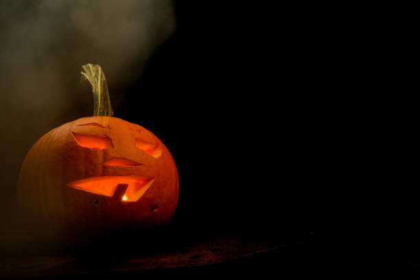istock Pumpkin with face carved into a jack o lantern on black background with smoke 1436528981