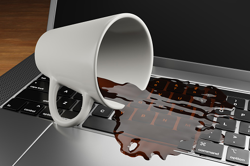 A cup of coffee spilled on the keyboard of a laptop. Illustration of the concept of stress at work and high stress work environment