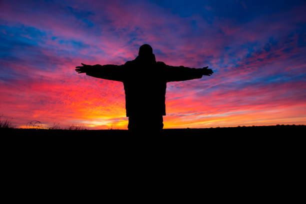 A man with outstretched arms silhouetted against a vibrant desert sunrise.