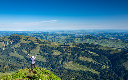 Senior woman with arms outstretched enjoying the view from the top of a mountain while hiking the Alps