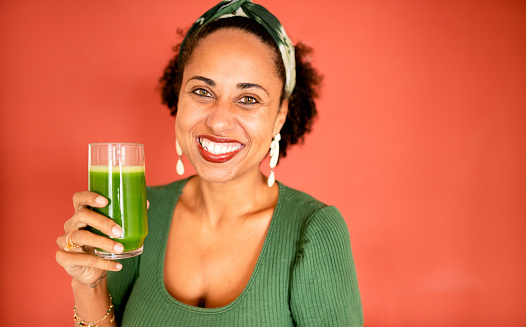 Portrait of a smiling woman holding a glass of fresh organic juice against a red background