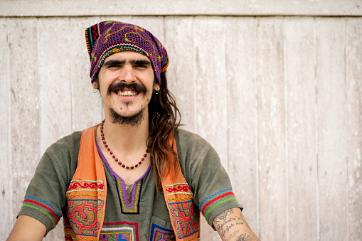 Portrait of a smiling hippie man wearing colorful clothes and headscarf sitting outside and looking at camera