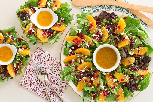 Spring mix lettuce topped with orange  supreme slices, pomegranate seeds, pistachios, and feta cheese served with a citrus dressing placed in the center of the salad to give the appearance of a wreath.