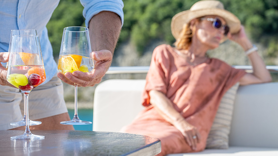 Close-up shot of glasses with drinks with fresh fruits. cropped view of male hands taking drinks away. Luxury vacation at sea.