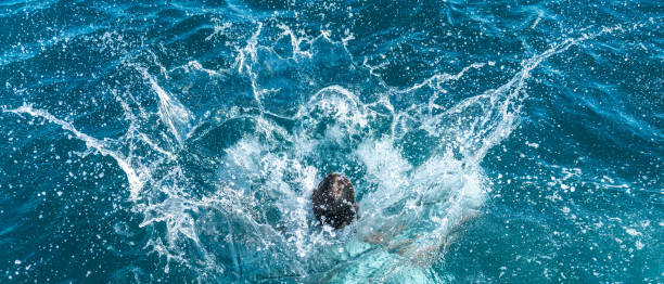 Big water splash after jumper hit water surface, only head visible. Hundreds of separated water drops flying in air. Luxury vacation at sea.