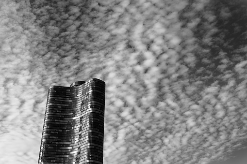 Black and white picture of a wavy, glass building underneath scattered clouds.