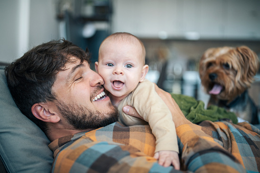 Idyllic scene with happy baby,father and dog laying on the couch at home.