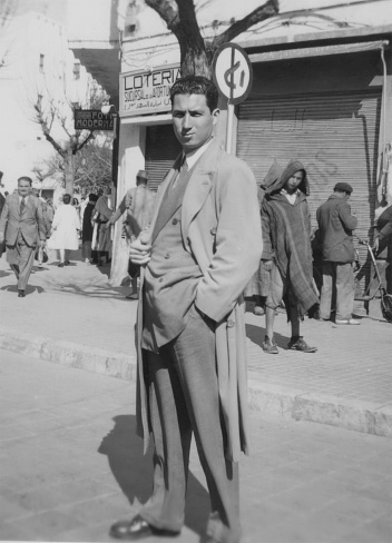 Black and white Image taken in the 40s: Elegant Young man wearing a suit standing in 1940s Tangier downtown