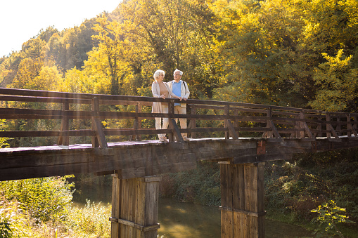 Active senior couple enjoying walk across the wooden bridge in the nature