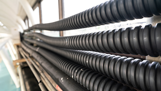 Row of electric cable protection flexible tube which are installed on factory workplace wall. Industrial equipment object photo, selective focus.