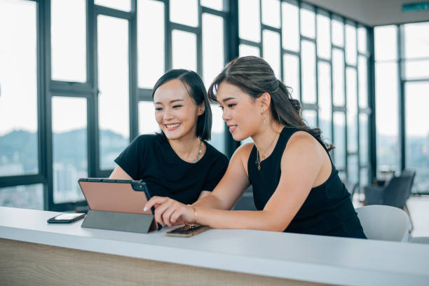 Two Asian Chinese women looking at ditigal tablet Asian and Indian Ethnicities, Friendship, Women, Mobile Phone, Happiness singapore cash stock pictures, royalty-free photos & images