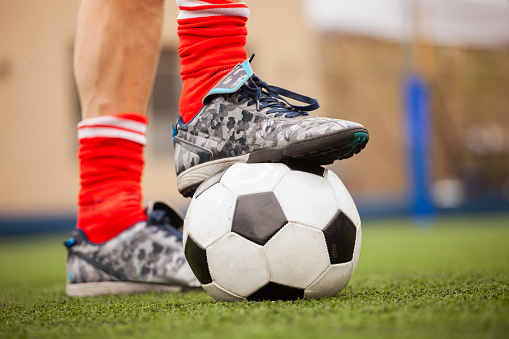 Close up of sport man's foot stepping on football ball at urban football pitch
