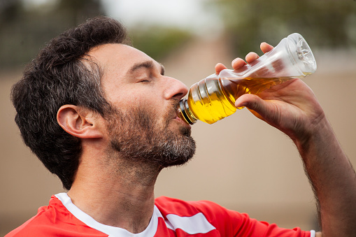 Side view of young adult man drinking sport drink during football training
