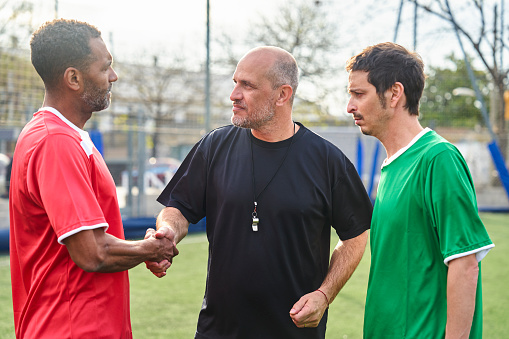 Mid-shot of referee at amateur soccer game shaking hands with both teams' players before starting game